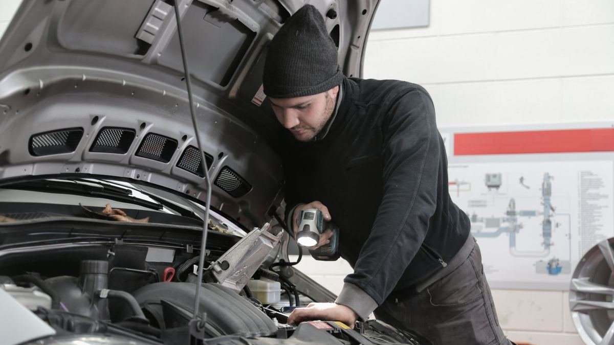 Person inspecting a car engine bay with a handheld torch in a garage
